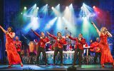 Performers dressed in red singing on a winter-themed stage against cool blue, red an green lighting.