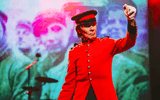 Performer in red military uniform on front of a background image featuring soldiers.