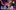 A group of young people joyfully cheering inside a colourful space with abstract shapes. The text 